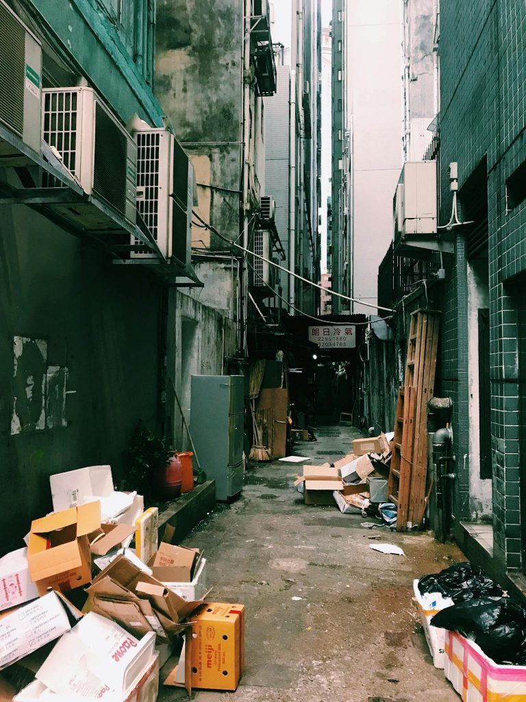 A narrow alley with air conditioners and scattered trash, reflecting urban lifestyle challenges.